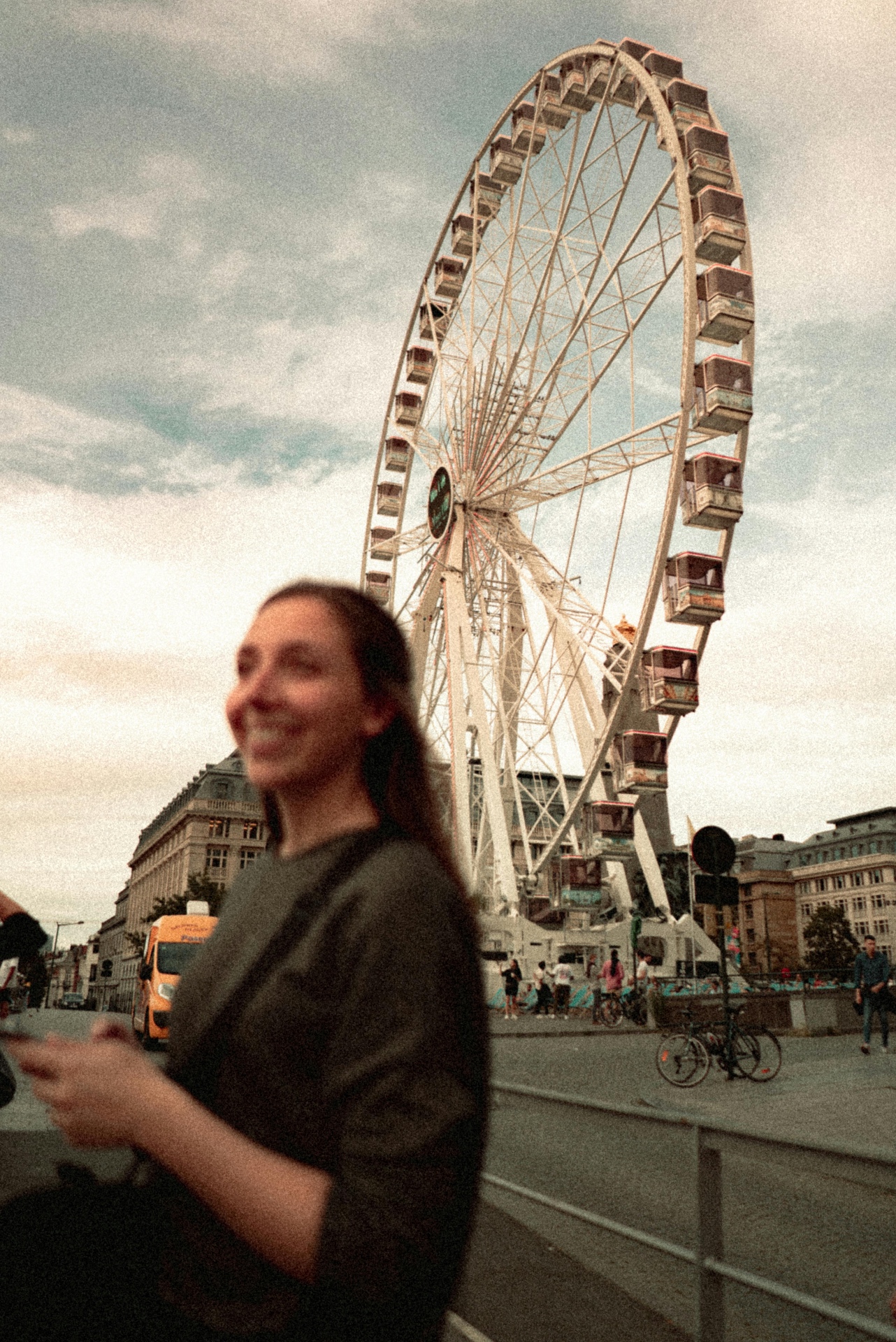 Grainy pastel street photo of a ferris wheel behind a smiling subject