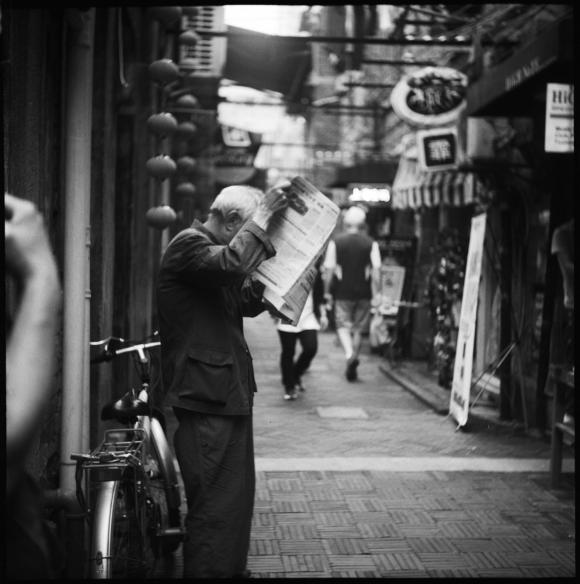 Black and white street photograph of a person reading a newspaper