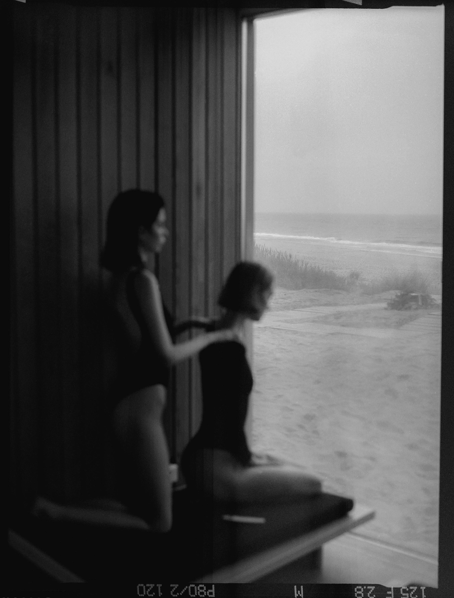 Black and white analog photograph of two people by a beach window
